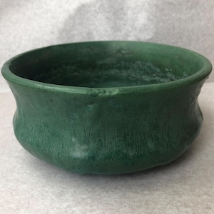 May include: A dark green ceramic bowl with a textured surface. The bowl has a wide, rounded shape with a slightly flared rim. The exterior has a matte finish.