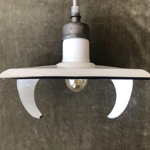 May include: A white enamel pendant light fixture with a black rim and a curved, open-sided shade design. The fixture features a central light bulb socket, a metallic gray top mounting component, and a glossy finish on the exterior surface.
