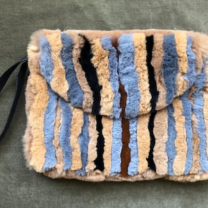 Puede incluir: Un bolso de mano de piel sintética a rayas con una correa negra. El bolso está hecho de diferentes tonos de piel sintética marrón, azul y negro.