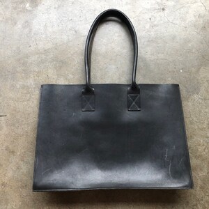 Puede incluir: Un bolso tote de cuero negro con dos asas superiores. El bolso tiene un dise&ntilde;o sencillo y est&aacute; hecho de un material de alta calidad.