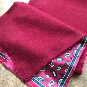 Könnte beinhalten: Ein burgunderfarbener Wollschal mit einem Paisley-Muster als Futter. Der Schal hat einen Fransenrand.