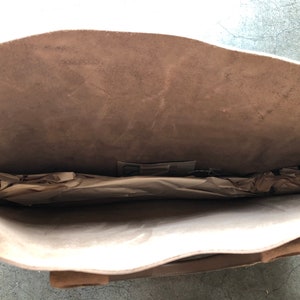 May include: A light brown leather tote bag with a zipper closure. The bag is open and the inside is lined with a light brown fabric. The bag is empty.