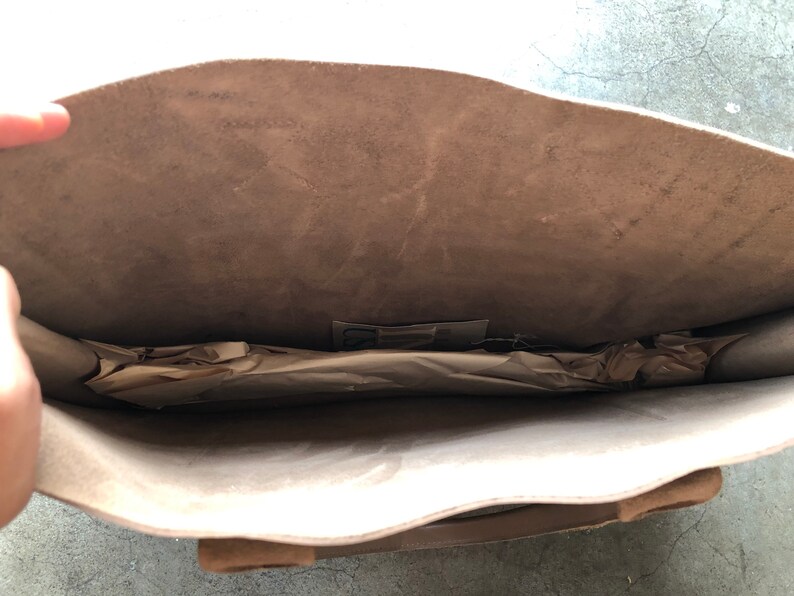 May include: A light brown leather tote bag with a zipper closure. The bag is open and the inside is lined with a light brown fabric. The bag is empty.