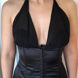 Pode incluir: Um corpete de cetim preto com um top halter de tule preto. O corpete tem um fecho de correr frontal e uma estrutura de varas.
