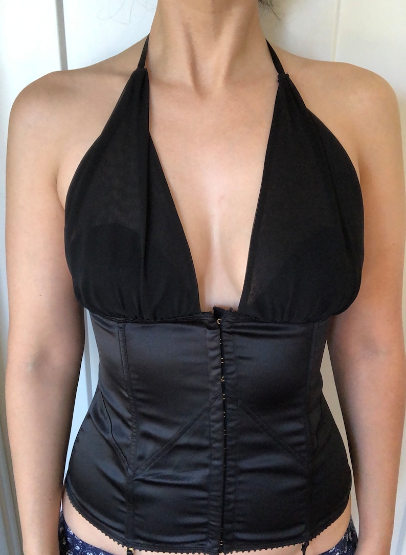 Pode incluir: Um corpete de cetim preto com um top halter de tule preto. O corpete tem um fecho de correr frontal e uma estrutura de varas.