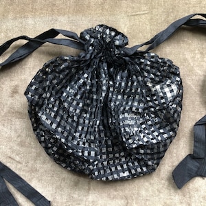 Pode incluir: Uma bolsa de cordão xadrez preta e prata com laços de fita preta.