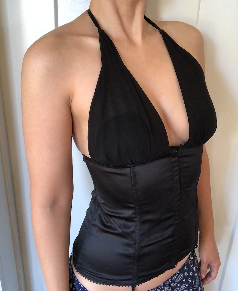 Pode incluir: Um corpete de cetim preto com um top halter e uma borda de renda. O corpete tem um decote em V profundo e um corpete com barbatanas.