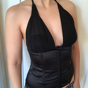 Pode incluir: Um corpete de cetim preto com decote halter e fecho de z&iacute;per. O corpete tem uma guarni&ccedil;&atilde;o de renda e &eacute; feito de um tecido macio e el&aacute;stico.