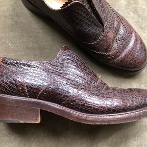 May include: A pair of brown leather shoes with a crocodile-embossed pattern. The shoes have a lace-up closure and a rounded toe.