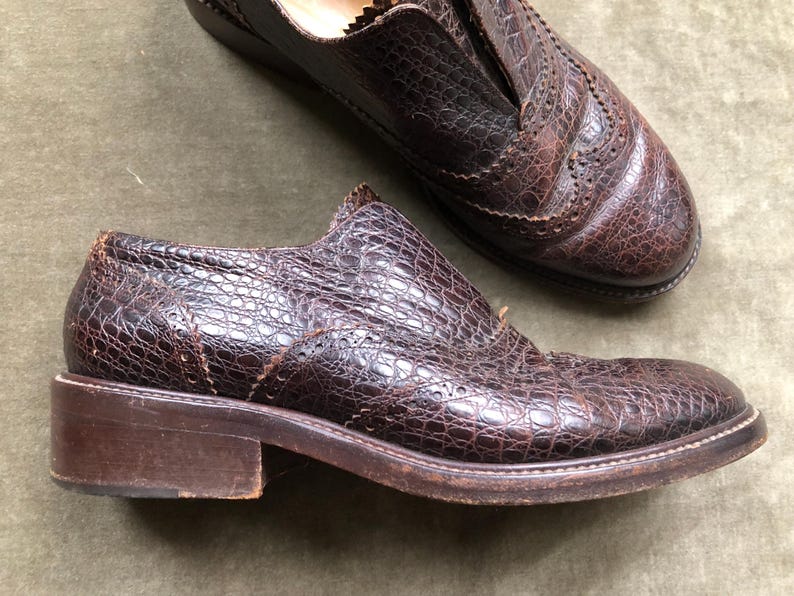 May include: A pair of brown leather shoes with a crocodile-embossed pattern. The shoes have a lace-up closure and a rounded toe.