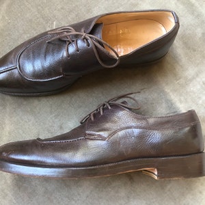 Puede incluir: Un par de zapatos marrones de cuero con cordones y punta puntiaguda. Los zapatos tienen un aspecto ligeramente desgastado y est&aacute;n hechos de cuero texturizado.
