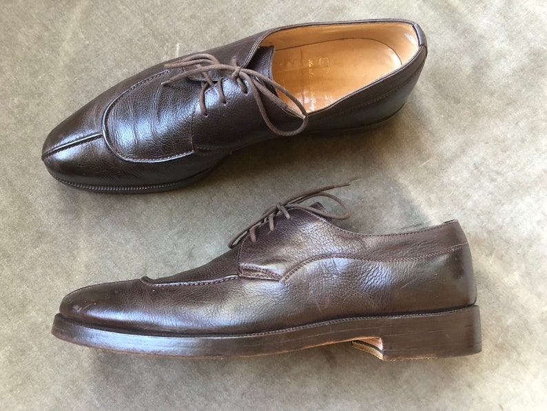 Puede incluir: Un par de zapatos marrones de cuero con cordones y punta puntiaguda. Los zapatos tienen un aspecto ligeramente desgastado y est&aacute;n hechos de cuero texturizado.