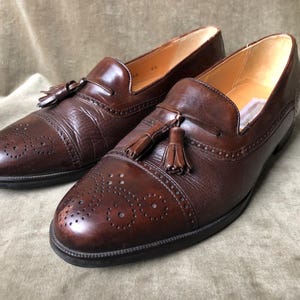 May include: A pair of brown leather tassel loafers with a wingtip design. The shoes have a brogue pattern and a tassel detail on the vamp.