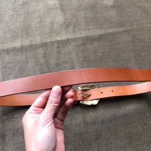 May include: A brown leather belt with a gold-toned buckle. The buckle has a decorative design.