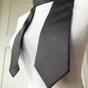 May include: A grey paisley patterned tie with a red and white design. The tie is on a white mannequin.