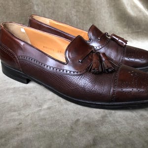 May include: A pair of brown leather tassel loafers with a wingtip design. The shoes have a brogue pattern and a tassel detail on the vamp.