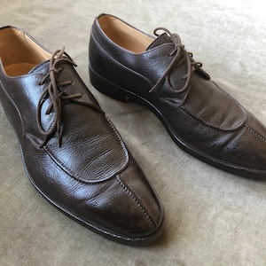Puede incluir: Un par de zapatos marrones de cuero con cordones y punta puntiaguda.