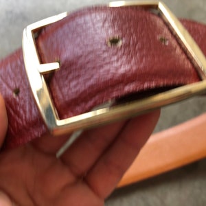 May include: A brown leather belt with a gold metal buckle. The buckle is rectangular with rounded corners and has a smooth, polished finish.