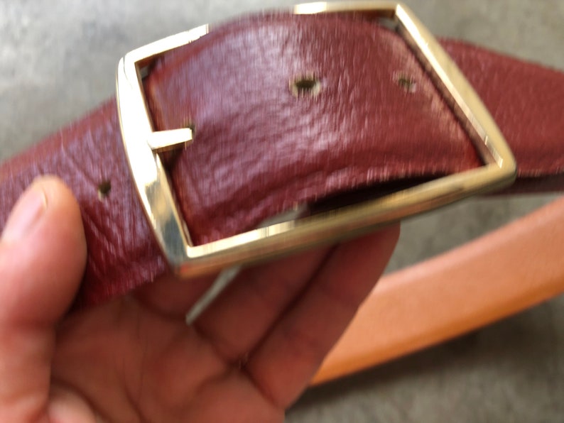 May include: A brown leather belt with a gold metal buckle. The buckle is rectangular with rounded corners and has a smooth, polished finish.