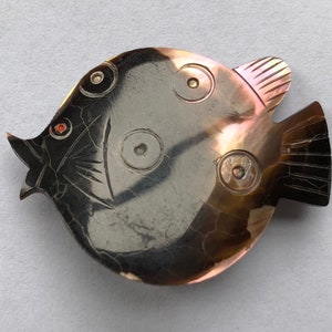 May include: A black and brown carved shell fish brooch with red eyes and gold accents.