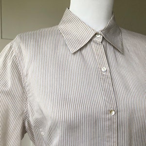 Puede incluir: Una camisa de manga larga a rayas con cuello abotonado y cierre de botones. La camisa está hecha de una tela ligera y tiene un corte holgado.