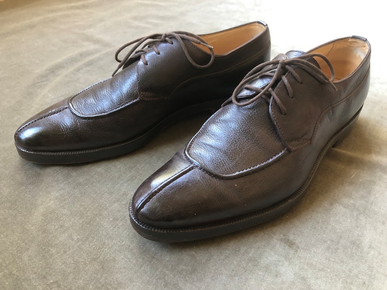 Puede incluir: Un par de zapatos marrones de cuero con cordones, punta puntiaguda y una costura decorativa en el empeine.