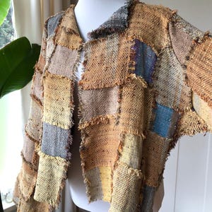 May include: A patchwork jacket made of woven fabric in shades of brown, beige, and blue. The jacket has a V-neck and a loose fit. The fabric is frayed at the edges, giving the jacket a rustic look.