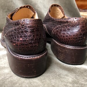 May include: A pair of brown leather shoes with a textured, alligator-like pattern. The shoes have a lace-up closure and a rounded toe.