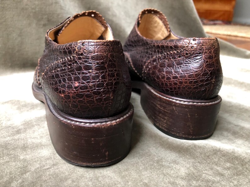 May include: A pair of brown leather shoes with a textured, alligator-like pattern. The shoes have a lace-up closure and a rounded toe.