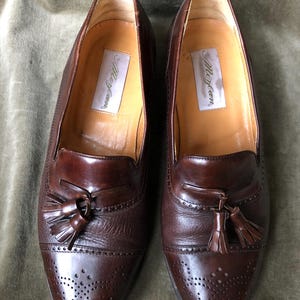 May include: A pair of brown leather tassel loafers with a brogue pattern and the text "Allen Edmonds" on the insole.