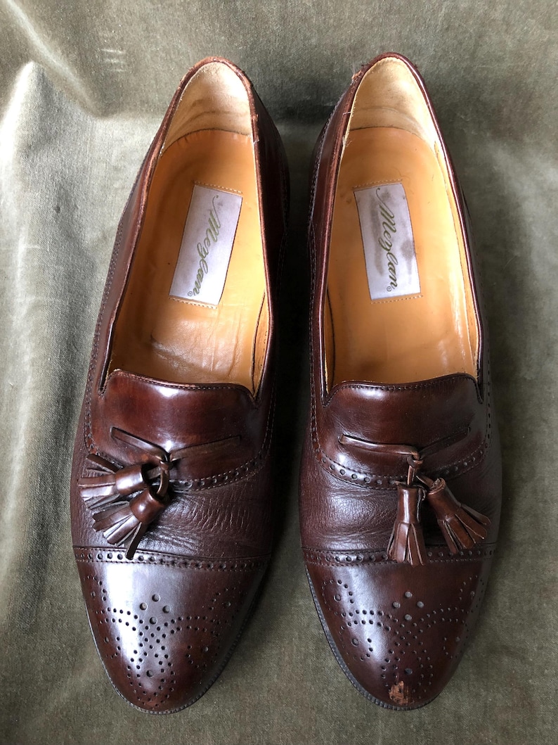 May include: A pair of brown leather tassel loafers with a brogue pattern and the text "Allen Edmonds" on the insole.