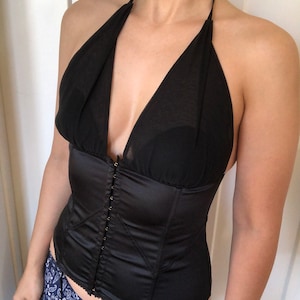 Pode incluir: Um corpete de cetim preto com decote halter e acabamento em renda. O corpete tem fecho de busk na frente e &eacute; feito de um tecido suave e sedoso.