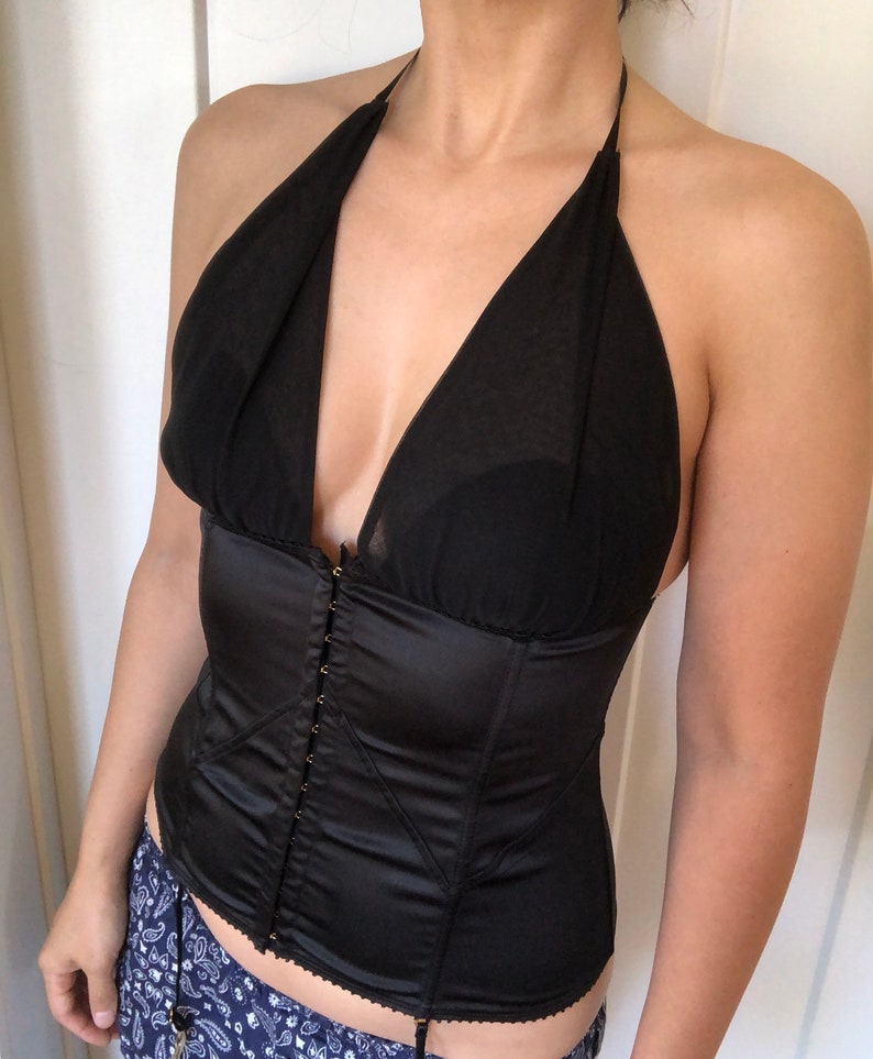 Pode incluir: Um corpete de cetim preto com decote halter e acabamento em renda. O corpete tem fecho de busk na frente e &eacute; feito de um tecido suave e sedoso.