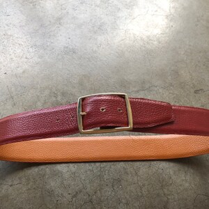 May include: A brown leather belt with a silver buckle. The belt has a tan leather lining.