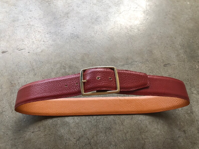May include: A brown leather belt with a silver buckle. The belt has a tan leather lining.