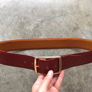 May include: A reversible leather belt with a gold-toned buckle. One side of the belt is brown leather, and the other side is burgundy leather.