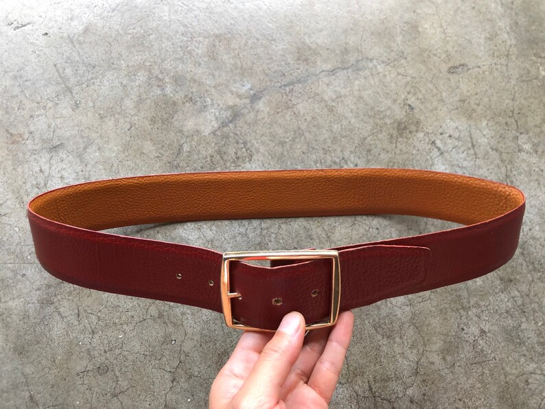 May include: A reversible leather belt with a gold-toned buckle. One side of the belt is brown leather, and the other side is burgundy leather.