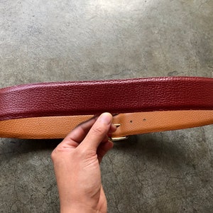 May include: A burgundy leather belt with a tan leather lining and a gold buckle.
