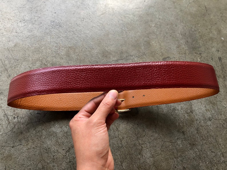 May include: A burgundy leather belt with a tan leather lining and a gold buckle.