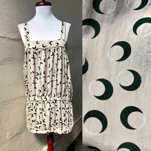 May include: A sleeveless dress with a cream background and a black crescent moon pattern. The dress has a gathered waist and a loose fit.
