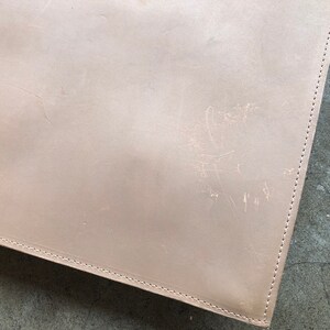 May include: A light brown leather portfolio with visible stitching around the edges.