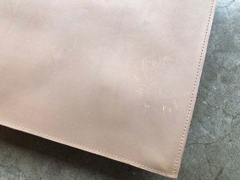 May include: A light brown leather portfolio with visible stitching around the edges.