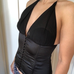 Pode incluir: Um corpete de cetim preto com decote halter e acabamento em renda. O corpete tem fecho de busk na frente e al&ccedil;as ajust&aacute;veis nas costas.