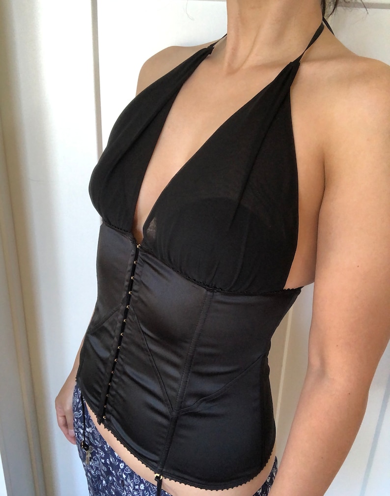 Pode incluir: Um corpete de cetim preto com decote halter e acabamento em renda. O corpete tem fecho de busk na frente e al&ccedil;as ajust&aacute;veis nas costas.