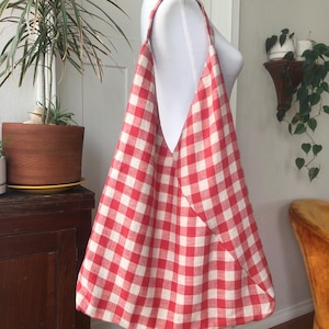 Op de afbeelding: Een rood-witte geruite draagtas op een mannequin. De stoffen tas heeft een groot, open ontwerp met lange bandjes. Het patroon is een klassieke ruit. De tas is geschikt voor het dragen van spullen.