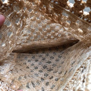 May include: Close-up of a beige crocheted bag with a pocket. The bag is made of a loosely woven, open-work material, creating a textured appearance. The pocket is visible inside the bag.