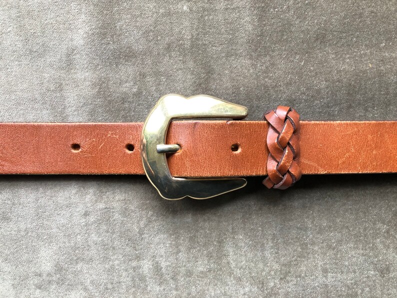 May include: A brown leather belt with a gold buckle and a braided leather strap detail.