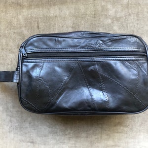 Op de afbeelding: Een zwarte leren reistas met een ritssluiting en een kort handvat. De tas is gemaakt van patchwork leer.