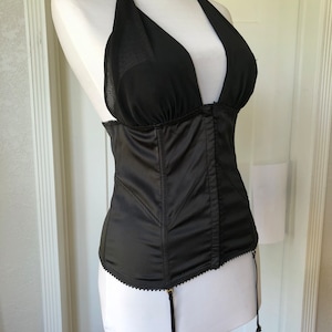 Pode incluir: Corpete de cetim preto com decote halter transparente e al&ccedil;as ajust&aacute;veis. O corpete tem um corpete com barbatanas e uma borda de renda. Possui ligas com ferragens douradas.