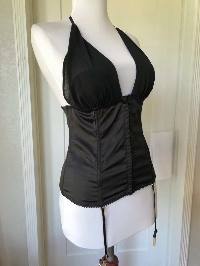 Pode incluir: Corpete de cetim preto com decote halter transparente e al&ccedil;as ajust&aacute;veis. O corpete tem um corpete com barbatanas e uma borda de renda. Possui ligas com ferragens douradas.